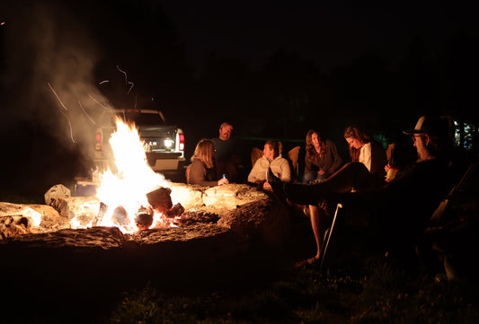 group of people sitting around a summer bonfire at a glampground
