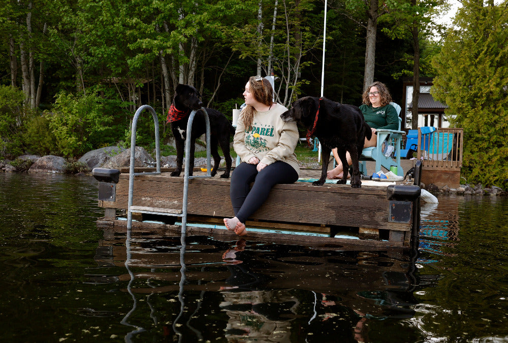 nomad crewneck on girl on the dock at the loon lake haus cottage with 2 black lab dogs