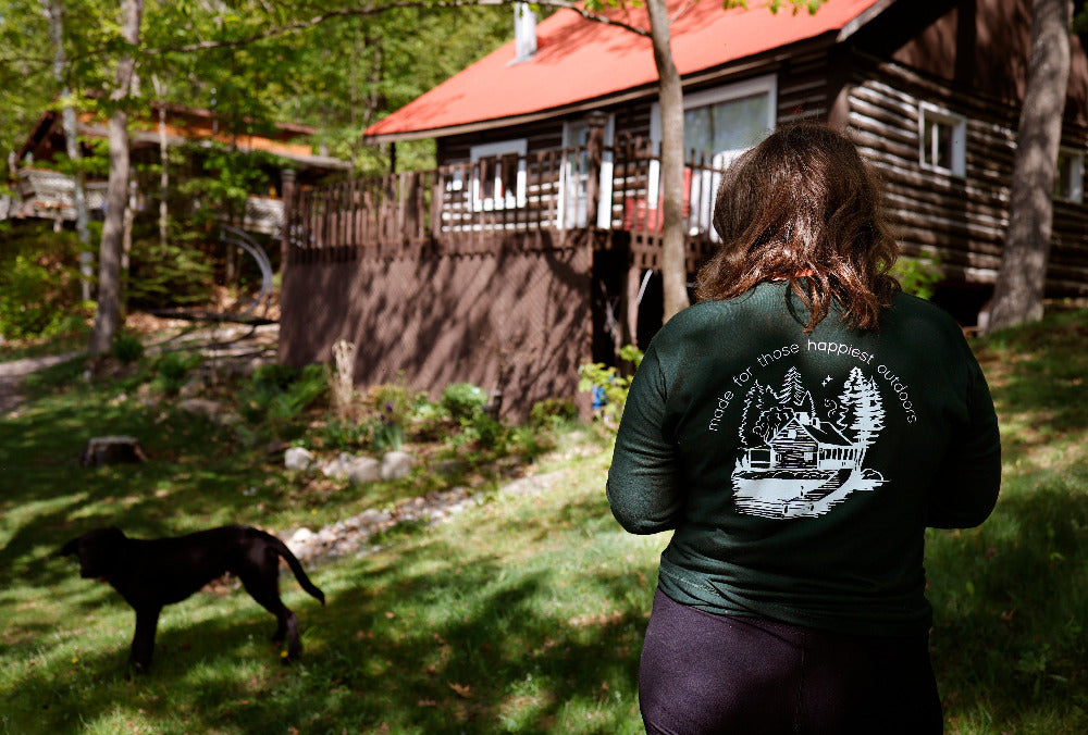 woman with black lab puppy at the cottage in long green cabin tee made for those happiest outdoors
